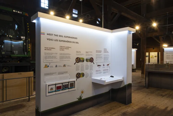 A slightly angled view shows an exhibition module with spinning blocks and the text “Meet the soil superheroes, voici les superhéros du sol”.