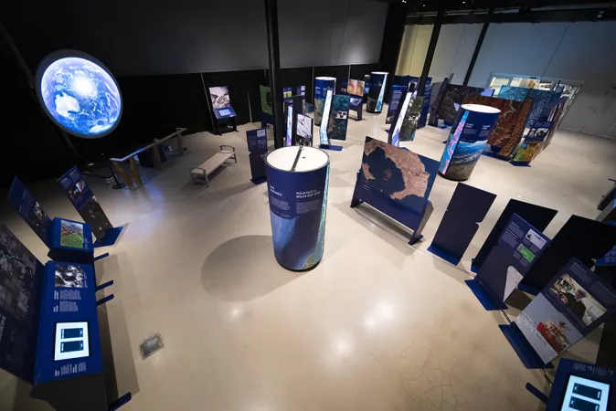 A wide view of an exhibition, with a number of exhibition modules which include circular towers, large graphic panels and a large circular screen.
