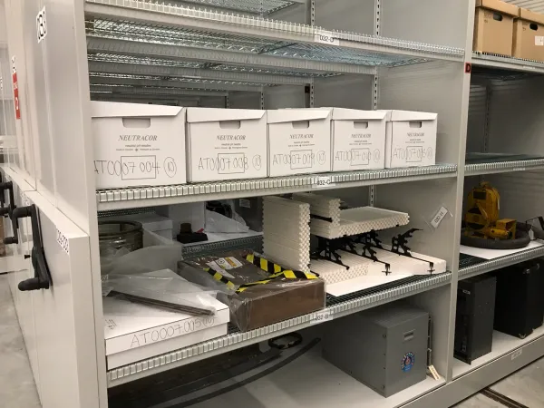 Plusieurs objets et boîtes blanches pour documents d’archives disposés sur une étagère de métal.
