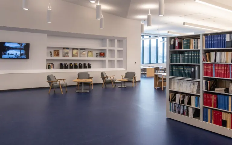 A brightly lit library with shelves full of books, a counter and armchairs