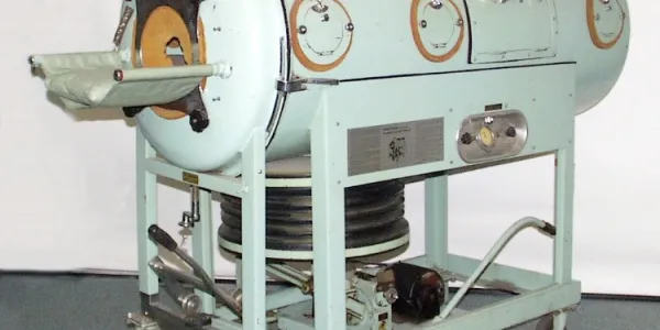 Une machine en métal, en forme de tube, avec une chambre de la taille d'une personne, utilisée pour permettre aux personnes atteintes de la polio et dont les muscles respiratoires sont paralysés de respirer.