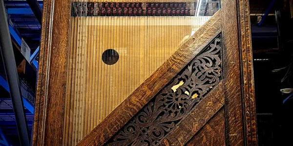 Gros plan de la harpe automatique Whitlock dans une salle d’entreposage de la collection. La photo montre en détail les cordes tirées sur la table d’harmonie en bois, le tout derrière une porte en vitre encadrée de bois sculpté.