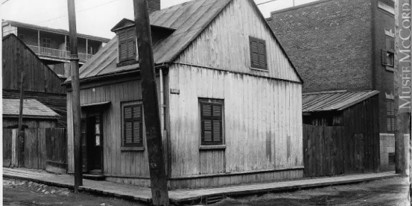 Une image noir et blanc montre une maison en bois dans un quartier ouvrier, au début des années 1900.]