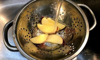 Un filet d’eau coule sur cinq tranches de pomme dans une passoire en métal.