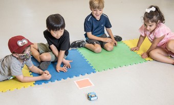Four young children sitting on the floor watching a Sphero Indi car drive over coloured mats.
