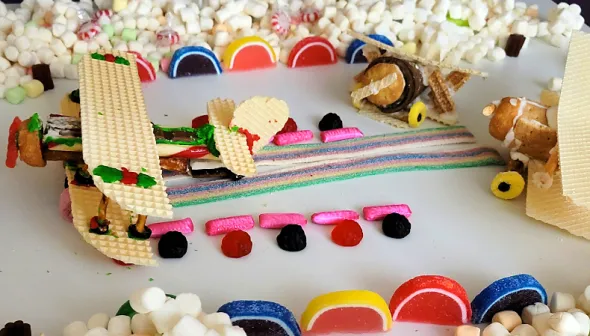 A tabletop is filled with edible treats; in the centre, aircrafts are made of cookies, icing, and candy.