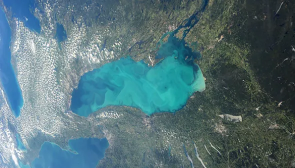 Photographie centrée sur le lac Ontario qui a une apparence turquoise trouble. L'image englobe des parties des lacs Huron et Érié le long de son côté gauche et le reste de l'image apparaît sous forme de végétation verte et de terre beige et brune.