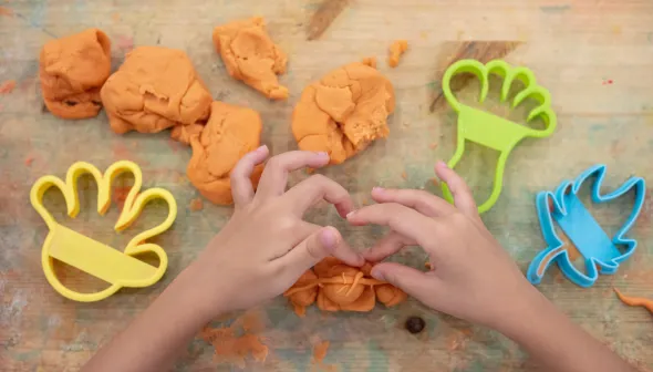 Une vue aérienne des mains d'un enfant jouant avec de la pâte à modeler orange sur une surface en bois. 