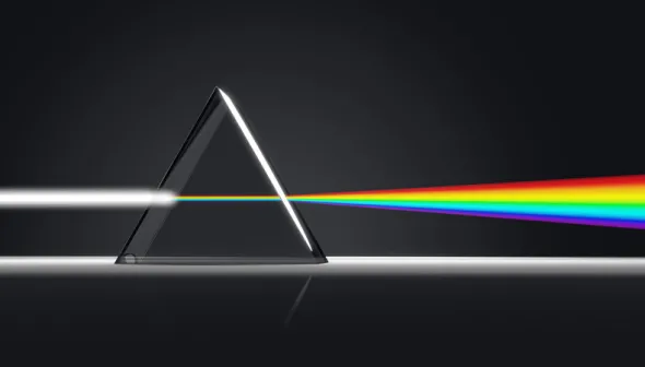 Sur un fond noir, un faisceau de lumière blanche traverse un prisme triangulaire et se transforme en un spectre de lumière colorée.