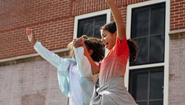 Deux pré-adolescentes se tiennent la main en sautant d'une plateforme d'environ 1 ½ pied de haut dans une école en dur.