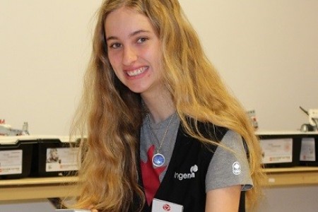 A young woman wearing a vest and name badge smiles at the camera.