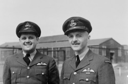 A black-and-white image of David Hornell standing next to Denny Denomy; both are wearing jackets with their pilot wings pinned on.