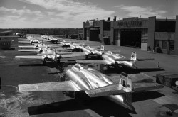 Photographie en noir et blanc montrant des avions à réaction CF-100 alignés devant deux hangars. 