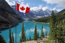 The Canadian flag, set against the backdrop of a clear, blue lake and mountains in Banff National Park, Alberta.