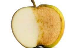 Une pomme à peau verte est coupée en deux devant un fond blanc. De la surface exposée de la pomme, la moitié et blanche, l'autre est brune. 