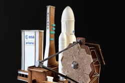 Deux créations en pain d'épice et en sucre sont représentées sur un fond sombre; une maquette du télescope spatial James Webb est au premier plan et la fusée Ariane 5 est visible à l'arrière-plan.