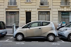 A small two-door grey electric vehicle parked on the street in front of a shop. 