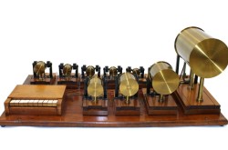 Table-top instrument featuring a small 10-key keyboard made of wood and ivory and ten cylindrical resonators made of brass. All are mounted on a wooden base.